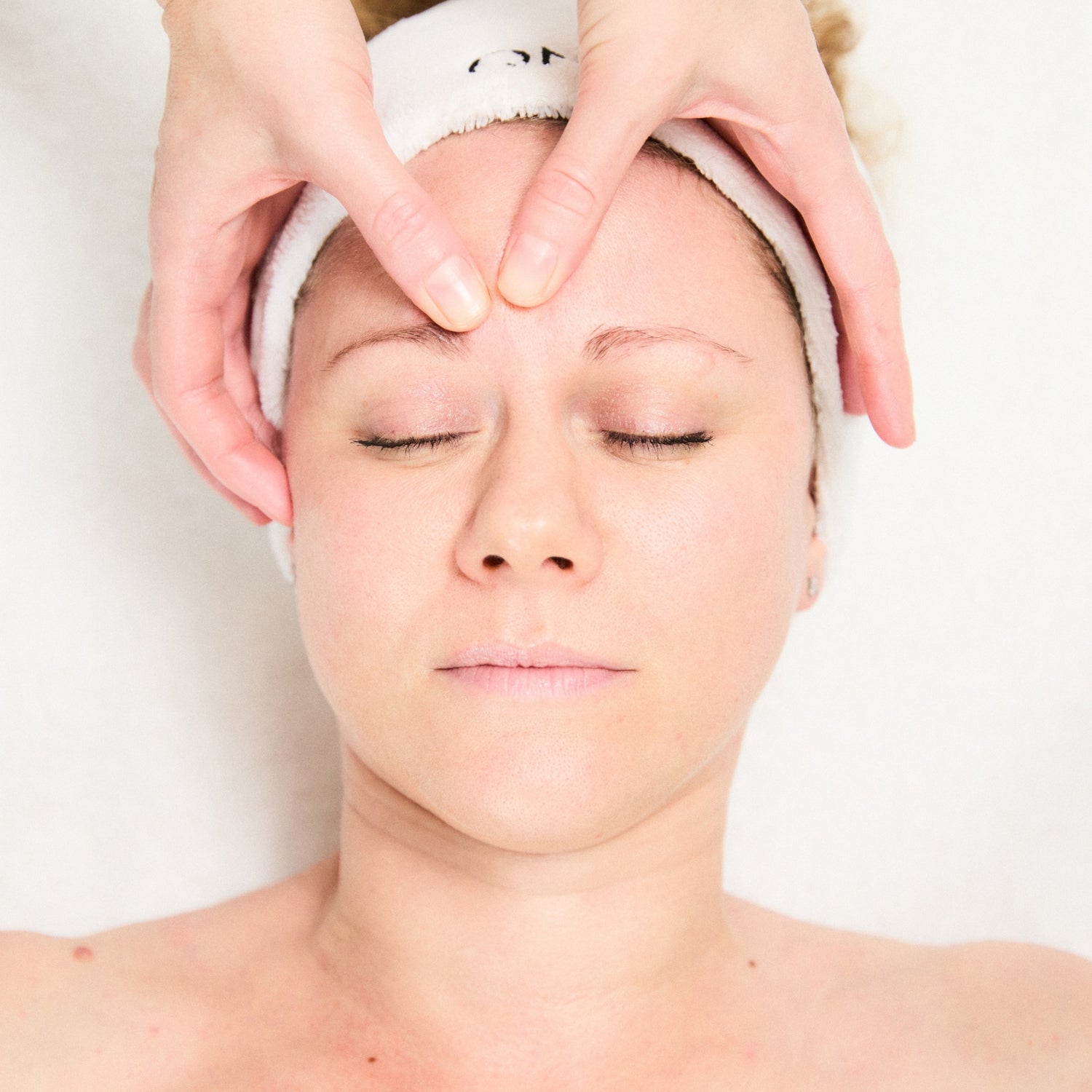 Person receiving a head massage with a white towel on a plain background