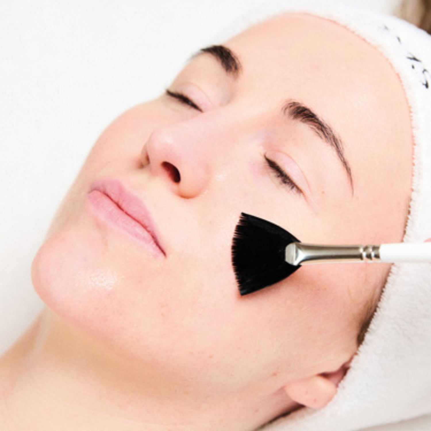 Person receiving a facial treatment with a brush on a white background