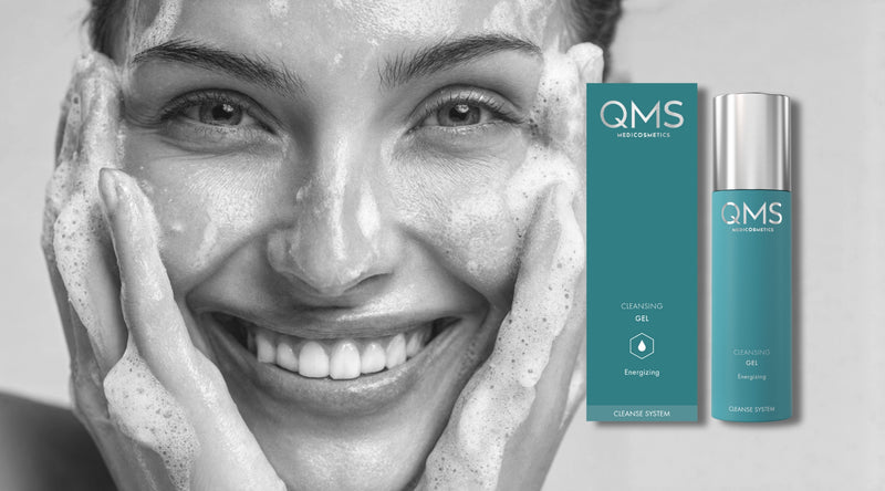 Woman with a smile showing teeth, with QMS Dermaceuticals skincare products on a gray background