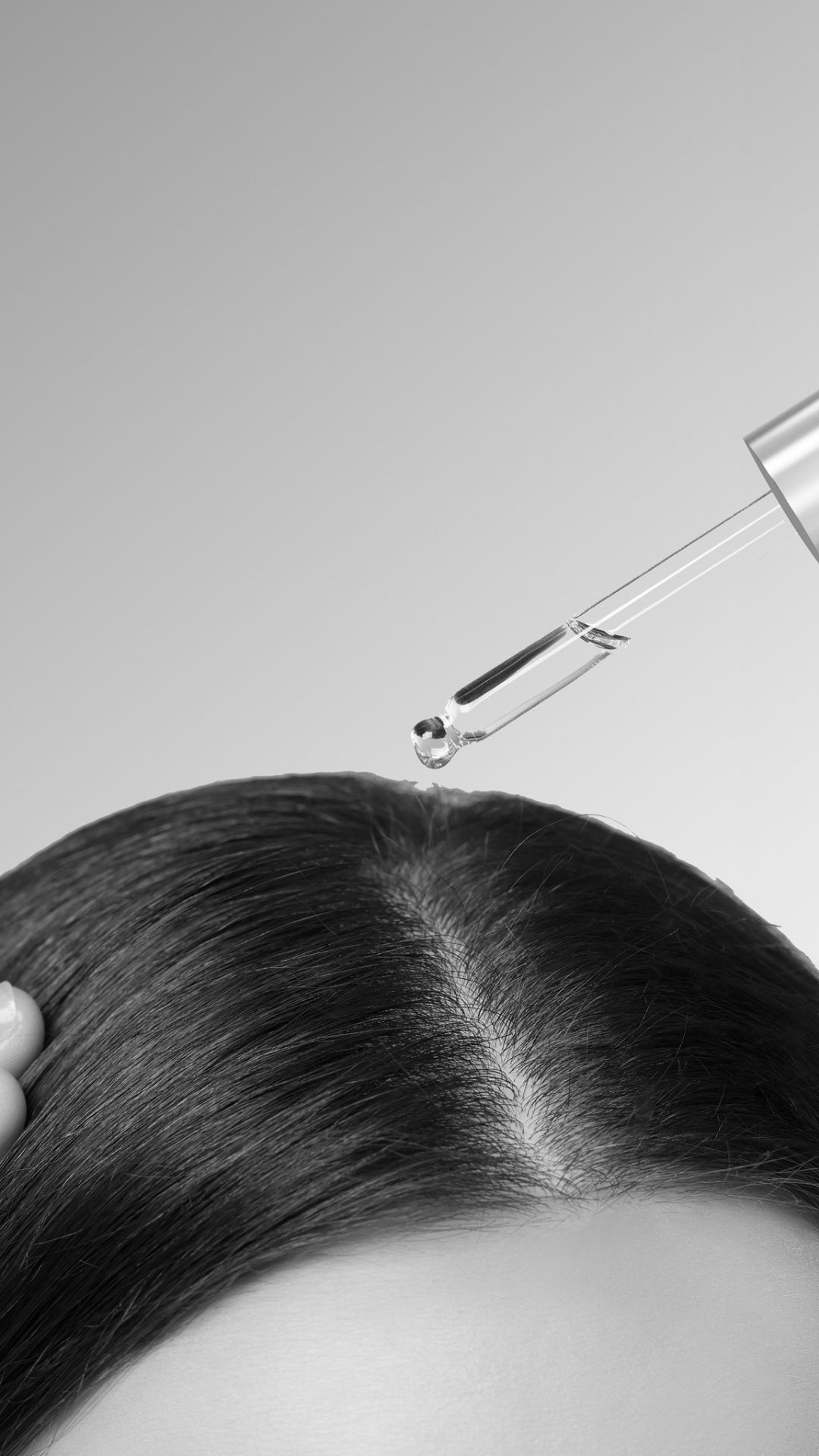 Close-up of a dropper applying a liquid to hair on a gray background